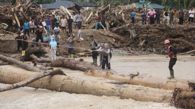 Sejumlah warga Tapanuli Selatan, Sumatra Utara menggunakan gelondongan kayu untuk menyeberangi sungai akibat banjir bandang yang menghatam wilayah tersebut. (Iba/Ist)